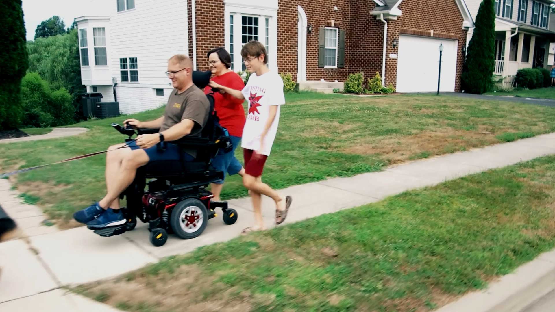Person in Motorized Wheelchair with Two People Walking